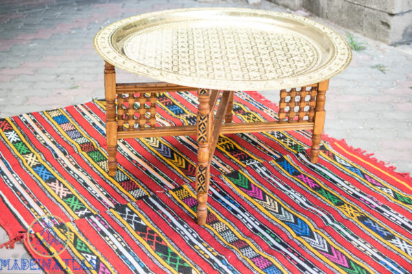 Moroccan brass coffee table with folding wood base setting on colorful rug