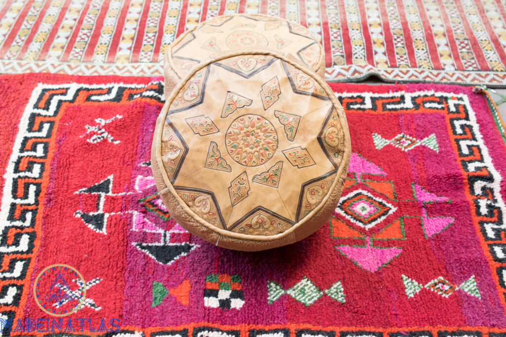 Leather vintage pouf carved with Amazigh tattoo stand on red vintage Berber rug