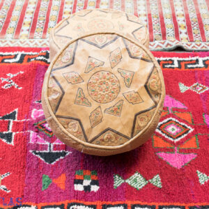 Pouf en cuir sculpté avec un tatouage amazigh sur un tapis berbère vintage rouge
