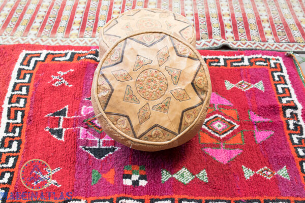 Hocker aus Leder geschnitzt mit Amazigh-Tattoo auf rotem Berberteppich